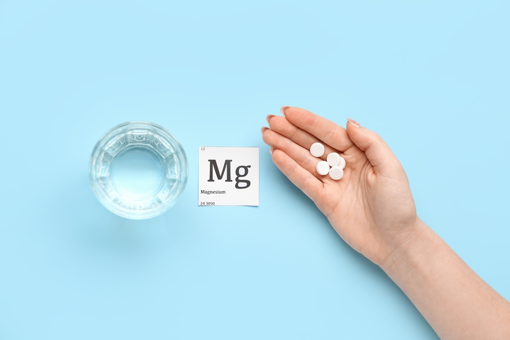 Female hand with magnesium pills and glass of water on blue background
