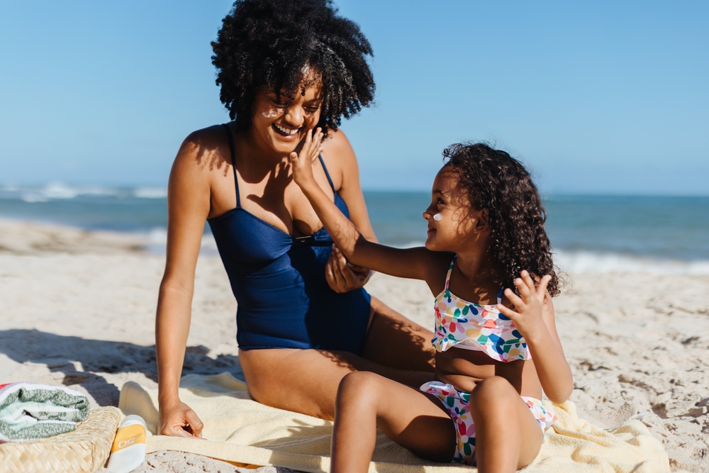 A joyful mother and daughter applying sunscreen while enjoying a sunny day at the beach, emphasizing family time and sun protection.
