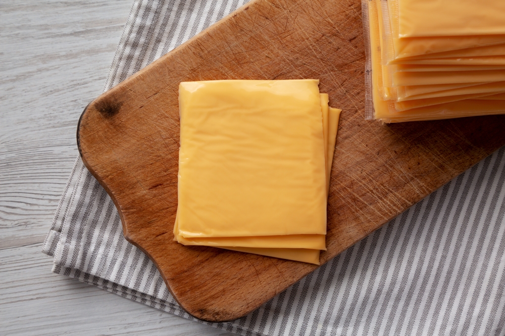 Yellow Cheddar American Cheese Stacked Slices on a wooden board, top view.
