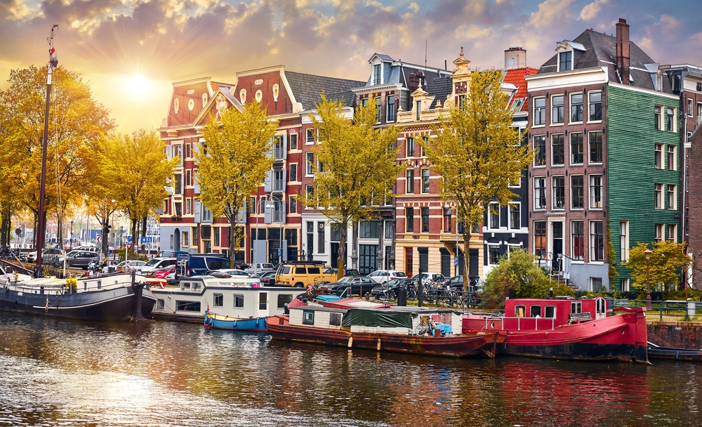Amsterdam, Netherlands. Panorama of famous dancing houses on river Amstel, water channels with house boats. Popular landmark and travel destination in old european city. Evening sunset landscape