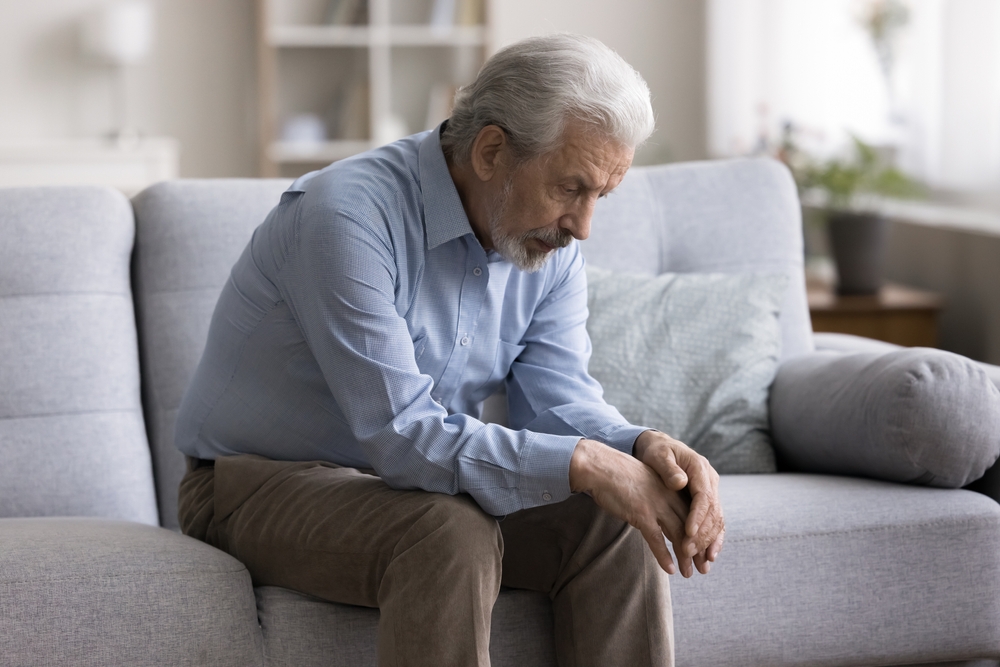 Pensive thoughtful older man sitting alone on couch at home, suffers from solitude, grief or loneliness, looks abandoned, goes through divorce or health problems. Retirement, dementia, senile disease
