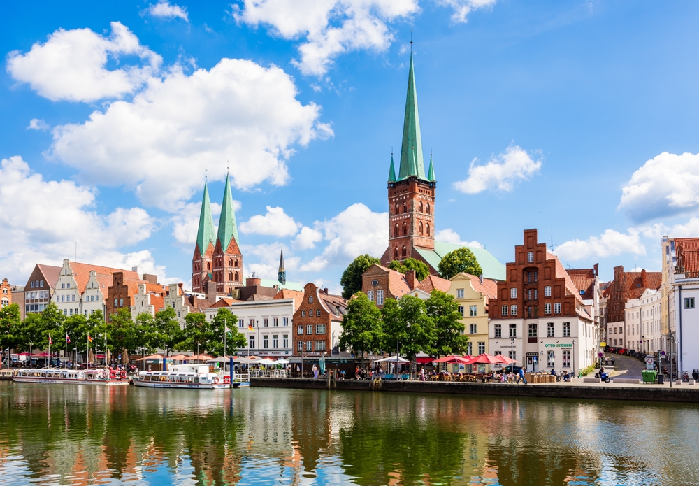 Lübeck, Germany - July 11, 2024: Riverfront of the historic center of the Hanseatic city seen from the Obertravebrücke, overlooked by the steeples of St. Peter (right) and St. Mary churches (left).