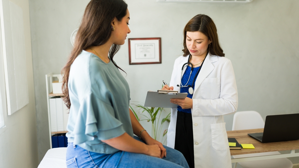 Caucasian doctor is carefully listening to her patient and taking notes on a clipboard during a medical consultation
