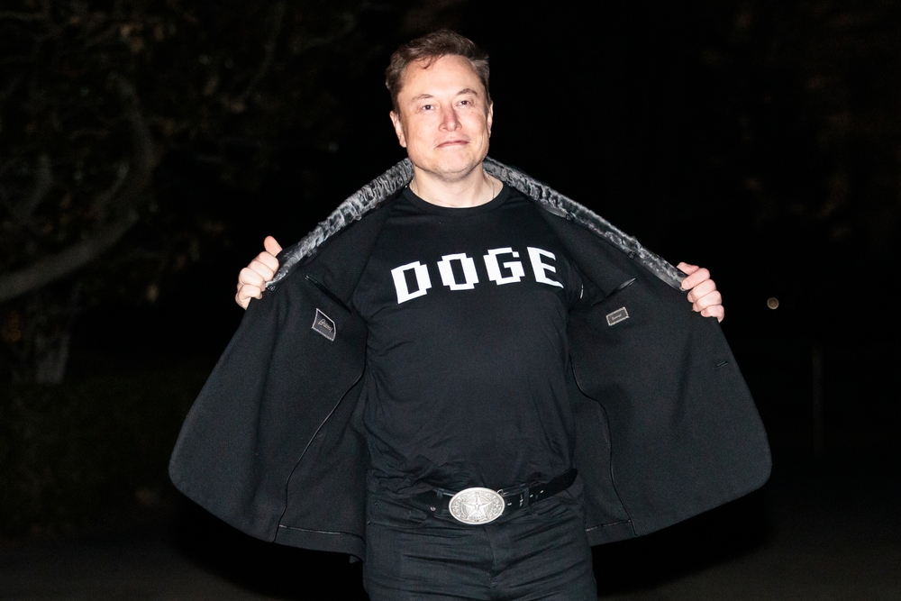 WASHINGTON – March 9, 2025: Elon Musk reveals a DOGE t-shirt and a Tesla belt buckle before entering the White House.
