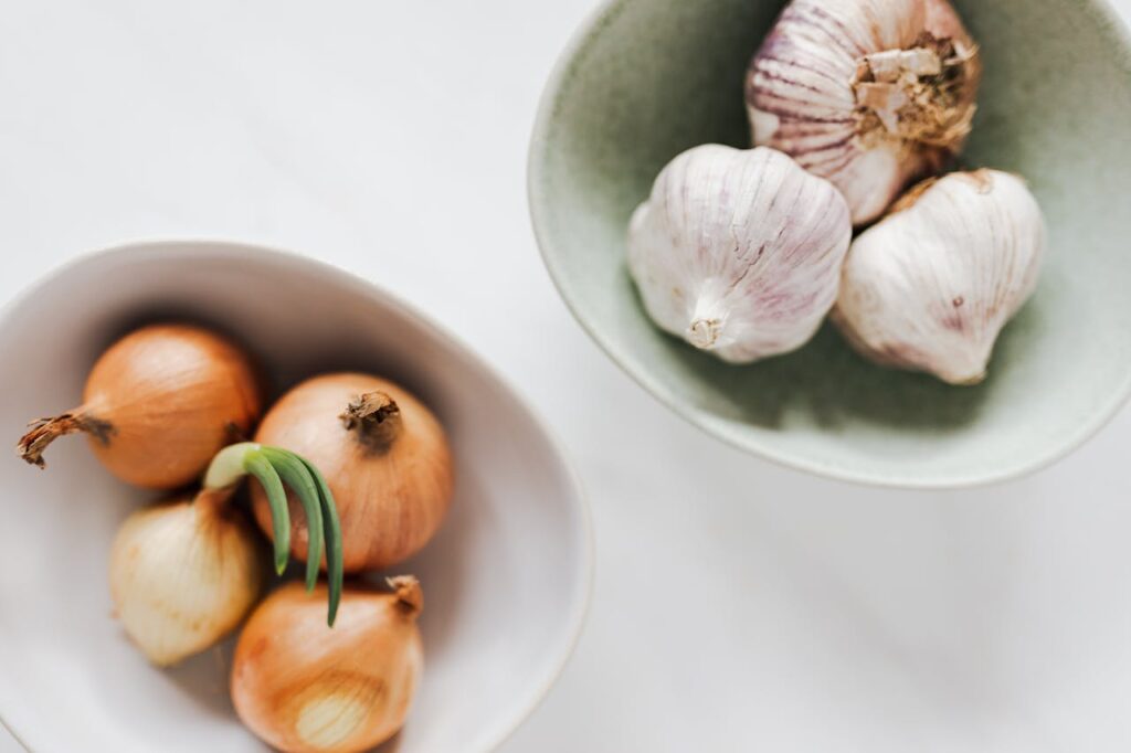 Bowls of garlic heads and onions on white table