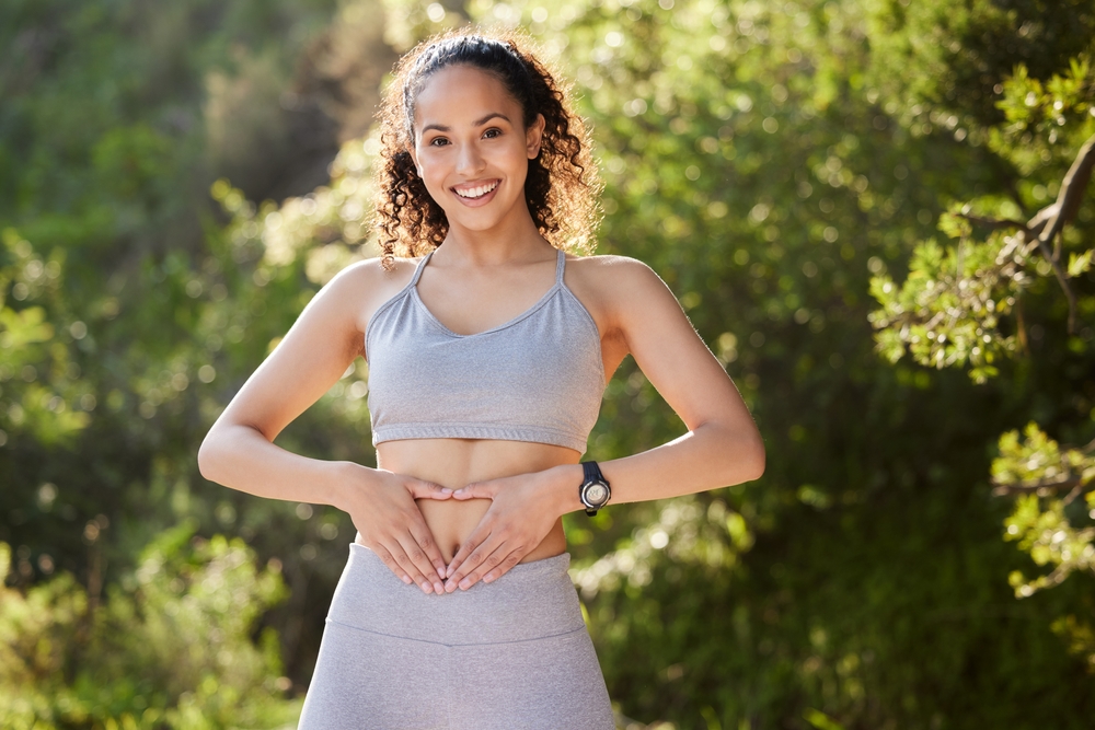Fitness, heart hands and portrait of runner woman outdoor in park for summer training or workout. Gut health, improvement and wellness with happy sports athlete running in nature for cardio exercise