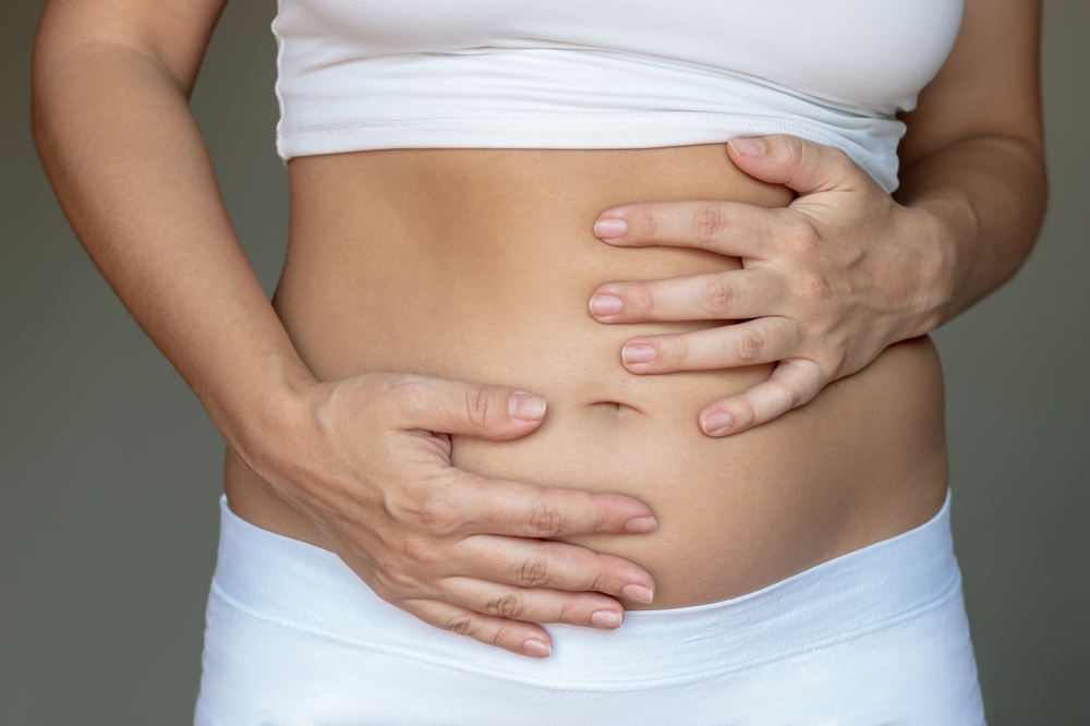 Stomach ache, bloating, flatulence, abdominal distension, colic, digestive disorders. A young woman holding her stomach with her hands on a dark gray background. Overeating, overweight, excess weight
