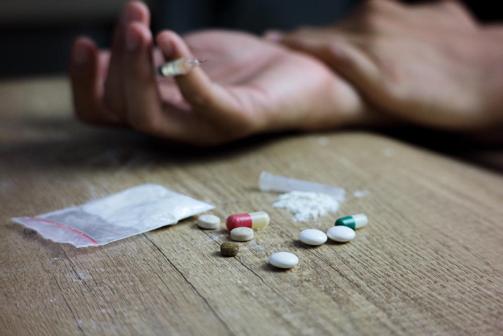 Young man or woman hand trying to reach and use drugs on wood table with syringe, methamphetamine, and pills. The concept for drugs addiction, International Day against Drug Abuse. say no to drugs
