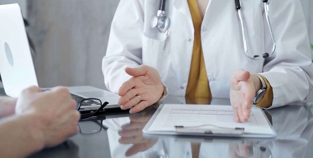 Doctor and patient consultation with clipboard and medication notes. Close-up view of unknown female doctor using a tablet during a patient consultation