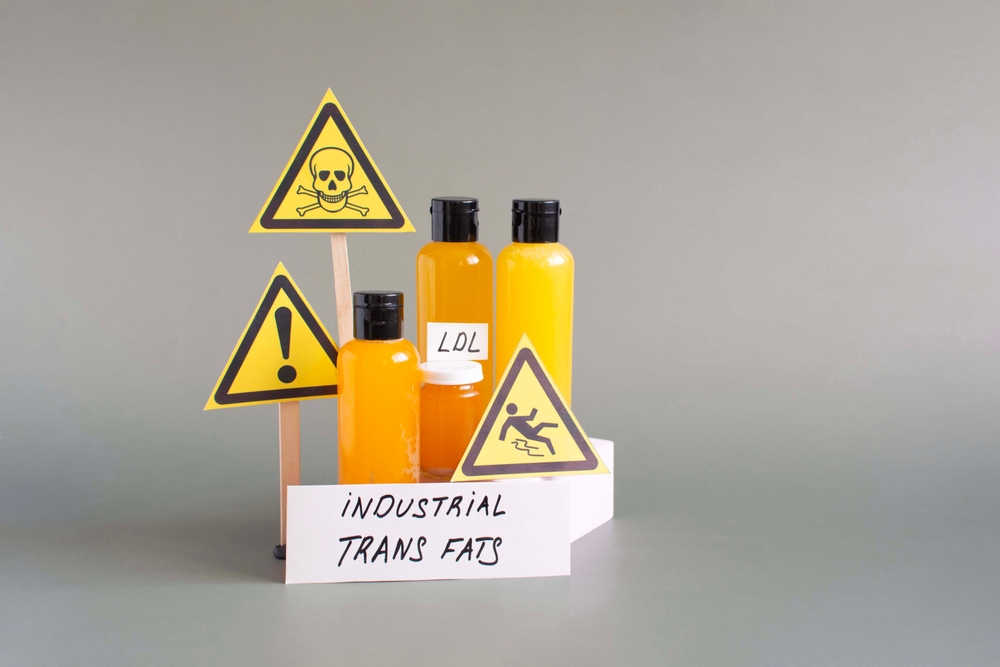 Containers filled with liquid containing trans fats, warning signs and the inscription "industrial trans fats"