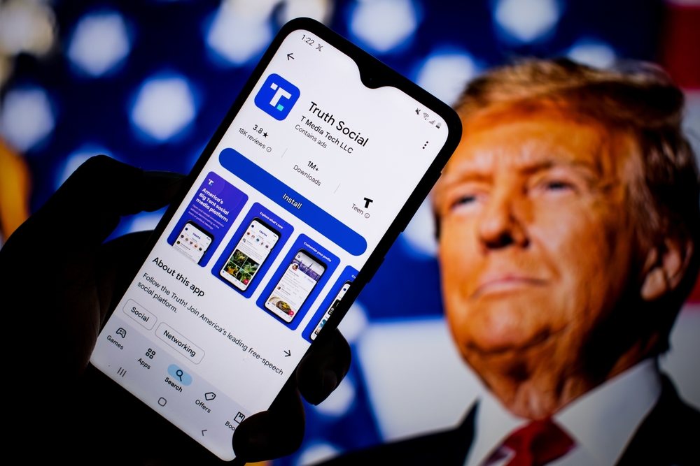 SEATTLE, WA, USA - APR 3, 2025: A man holds smartphone with Truth Social app on Google Play and the face of US president Donald Trump in the background. The app is owned by TMTG.