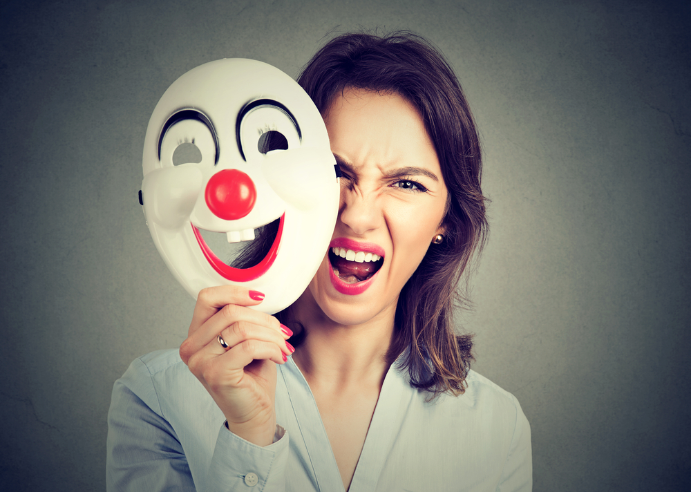Portrait angry screaming woman taking off happy clown mask isolated on gray wall background. Negative human emotions feelings 