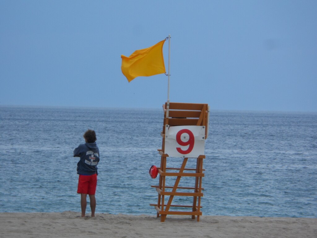 Yellow flag on lifeguard chair at beach warning of moderate hazards and developing currents that require caution.