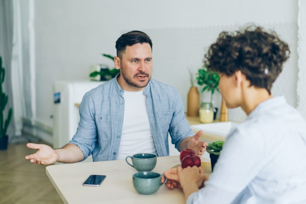 Man and woman sit at table having serious conversation, one gesturing while speaking