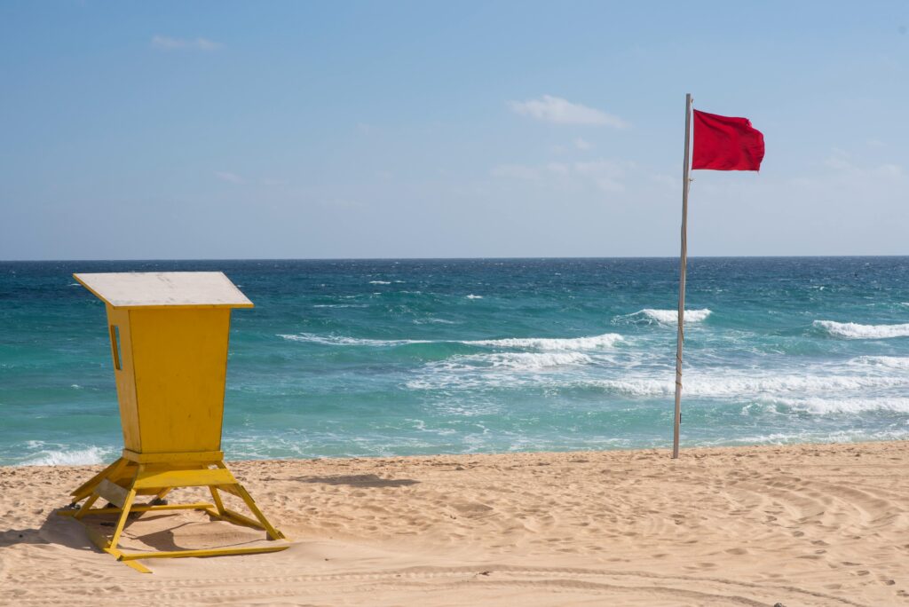 Red flag posted on beach with active waves signaling high hazard conditions where swimming is discouraged.