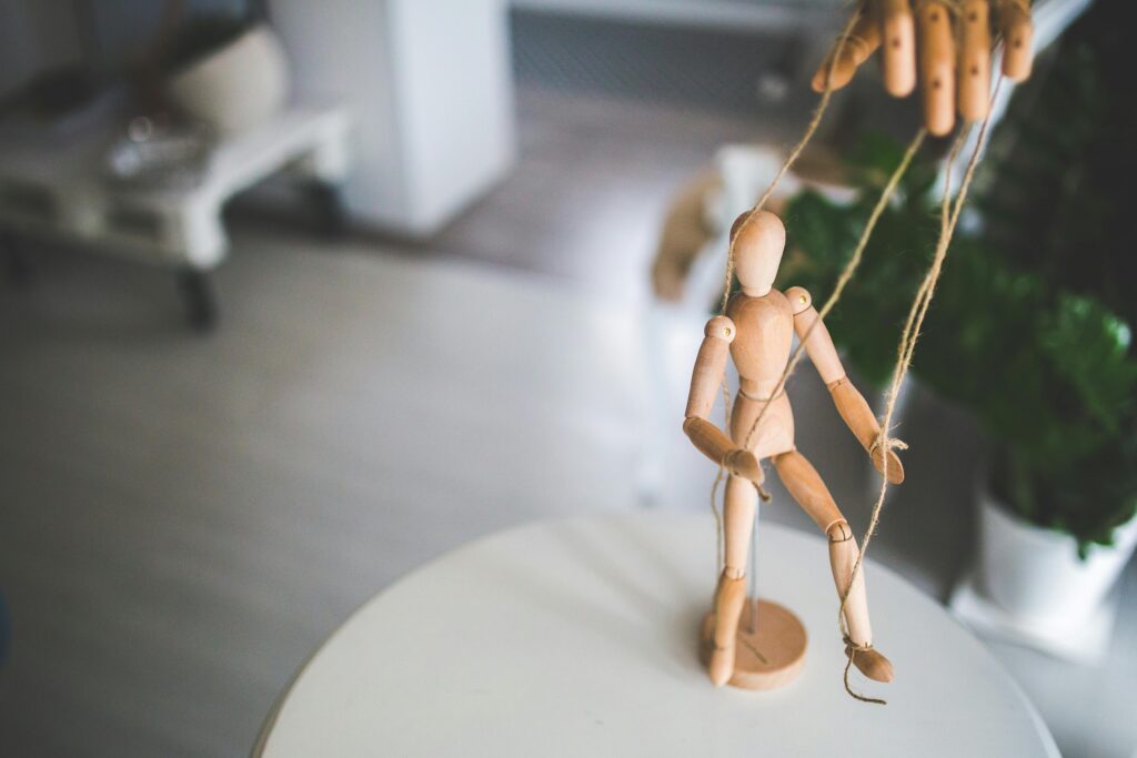 Hands control wooden puppet figure with strings, showing manipulation concept