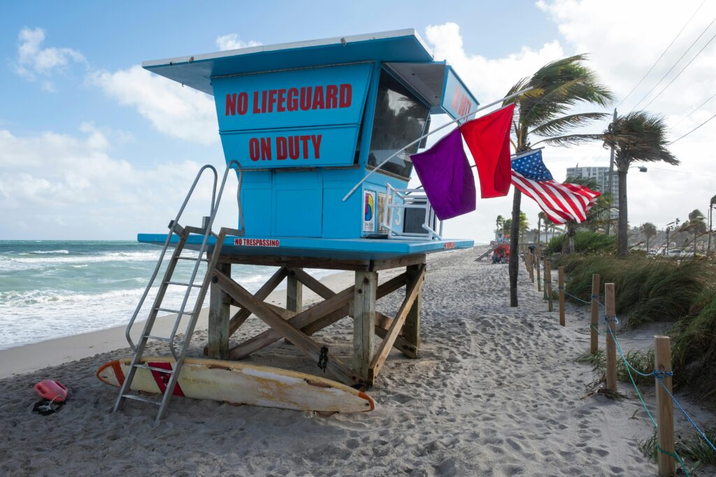 Lifeguard station displaying purple and red flags with "NO LIFEGUARD ON DUTY" sign, warning of marine life presence and high hazards.