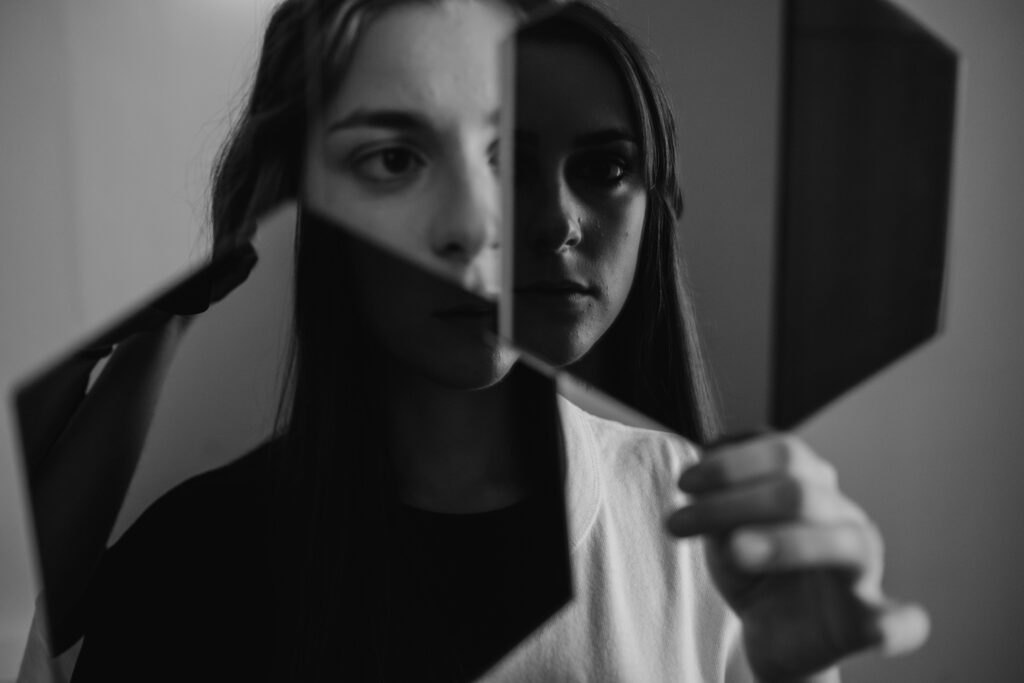 Woman holds two mirrors to her face, showing fragmented reflection in black and white, representing reality distortion from things narcissists say