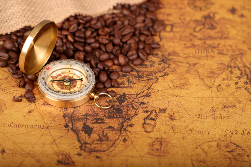 Coffee Beans and Vintage compass on an old world map - trade and explorer concept 