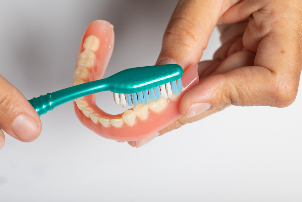 Doctor Dentist show how to Cleaning dental prosthesis with toothbrush, hold denture in hand