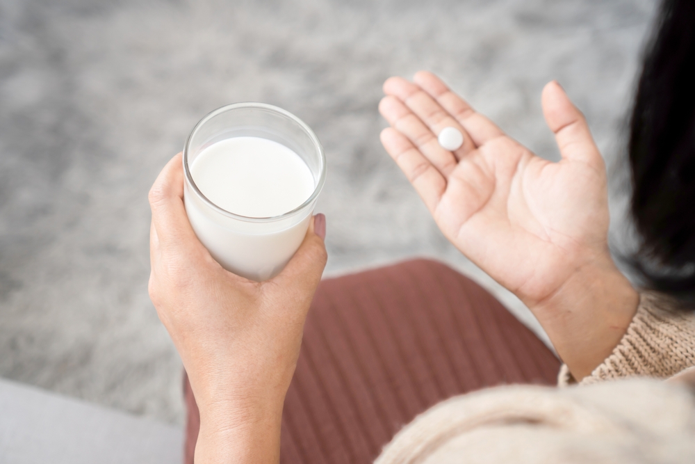 closeup woman taking medicine hand holding a glass of milk