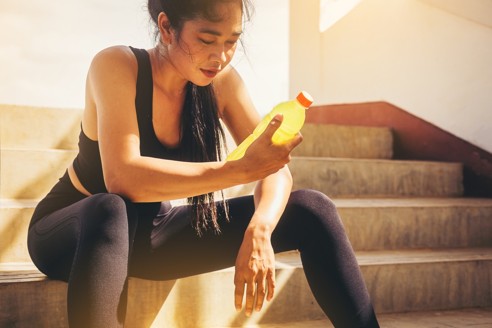 Tired runner woman with a bottle of electrolyte drink freshness after training outdoor workout at the stadium stairway.