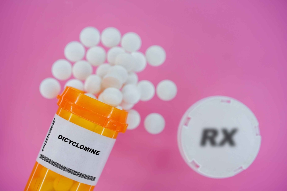 Dicyclomine Rx medicine pills in plactic vial with tablets. Pills spilling from yellow container on pink background.