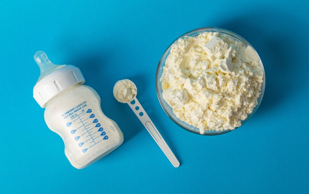 Baby bottle with milk for feeding. A plate with dry milk mixture with bifidobacteria, protein component and oligosaccharides. Blue background