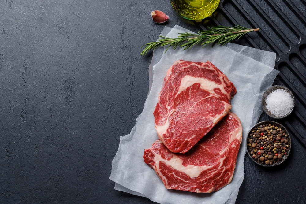 Raw ribeye steaks with savory spices. Flat lay with copy space