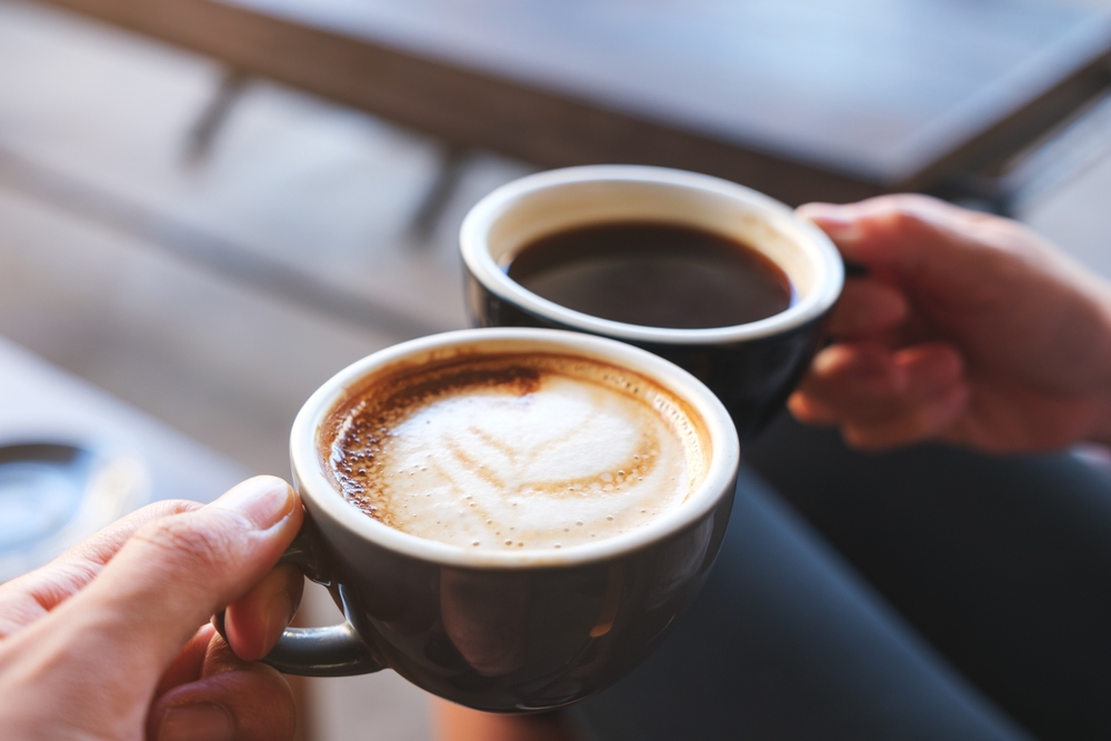 Closeup image of a man and a woman clinking coffee mugs in cafe