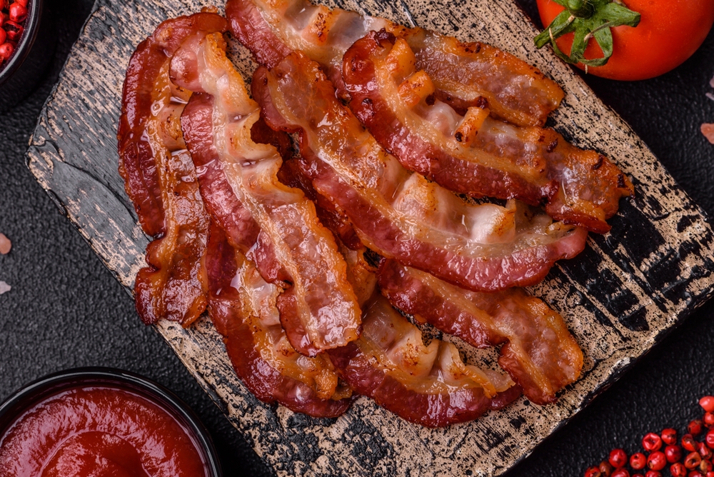 Delicious fresh fried bacon with salt and spices on a dark background as an ingredient for preparing a hearty breakfast