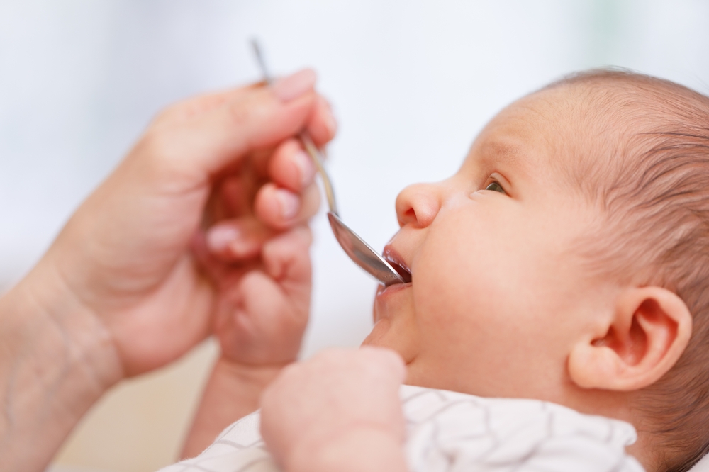 Mother feeding newborn baby with vitamin or liquid medicine using spoon