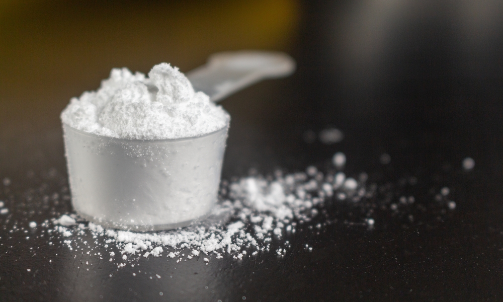 Creatine powder in a measuring scoop, pre-workout for gym on black wooden background.