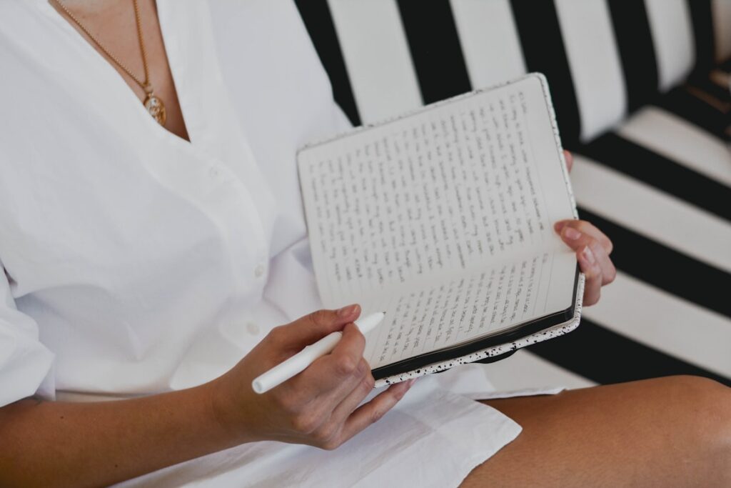 Hands holding open book while sitting on a couch with a striped pattern.