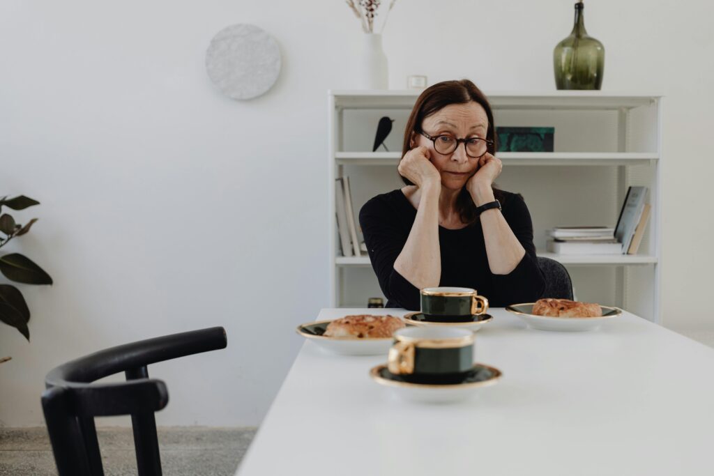 Older woman looking stressed at table set for two with untouched food.