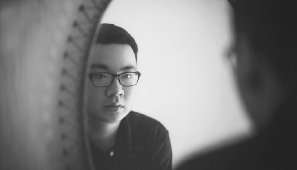 Person looking at own reflection in mirror wearing glasses.