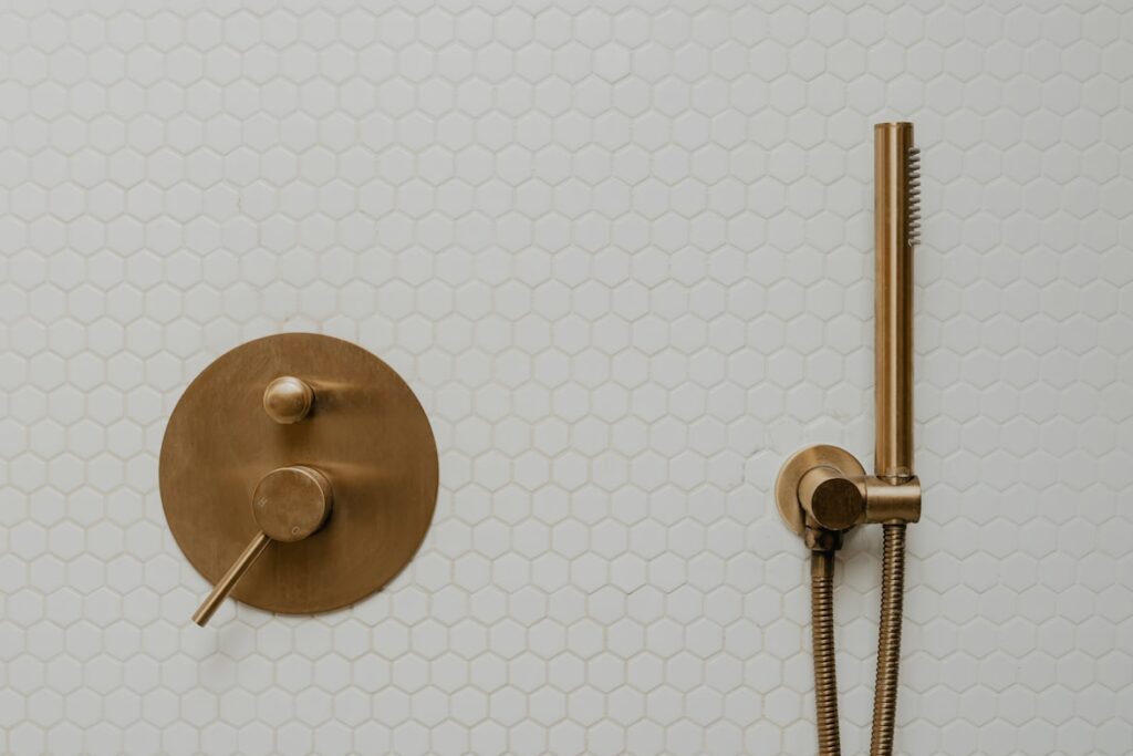 Gold shower fixtures with a detachable head on white hexagonal tile.