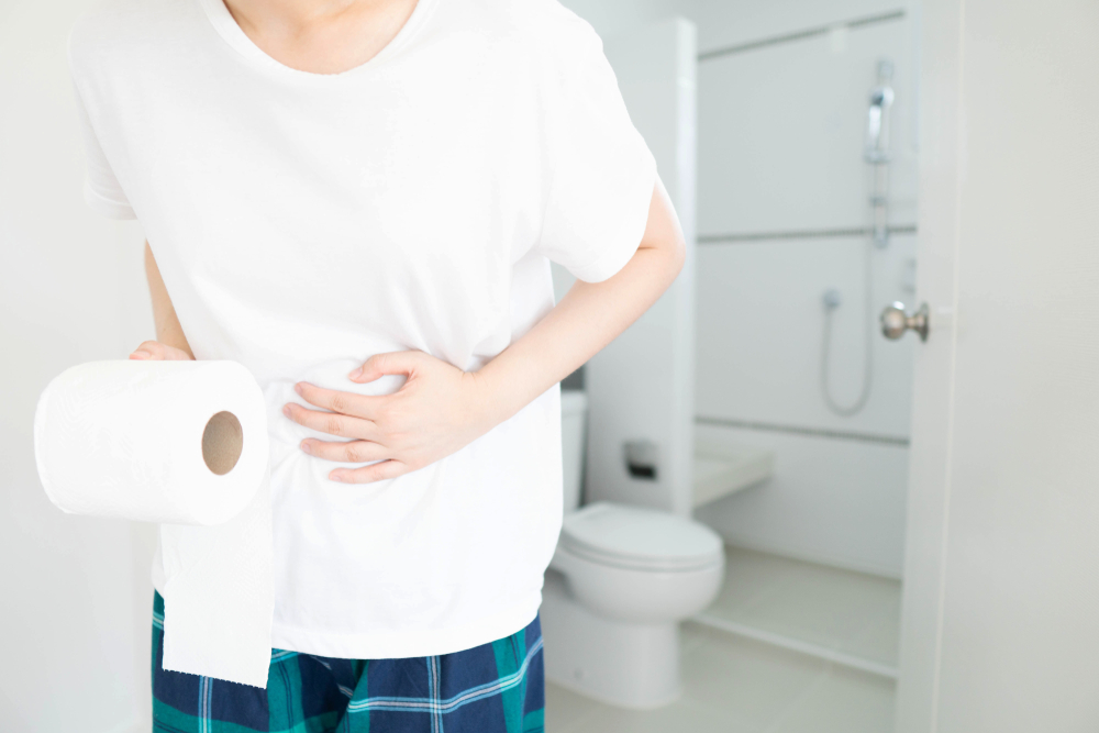 Young woman suffering form abdominal pain and holding toilet tissue paper roll in front of the bathroom at home. Concept of constipation, diarrhea, hemorrhoid, food poisoning or IBS. Health care.