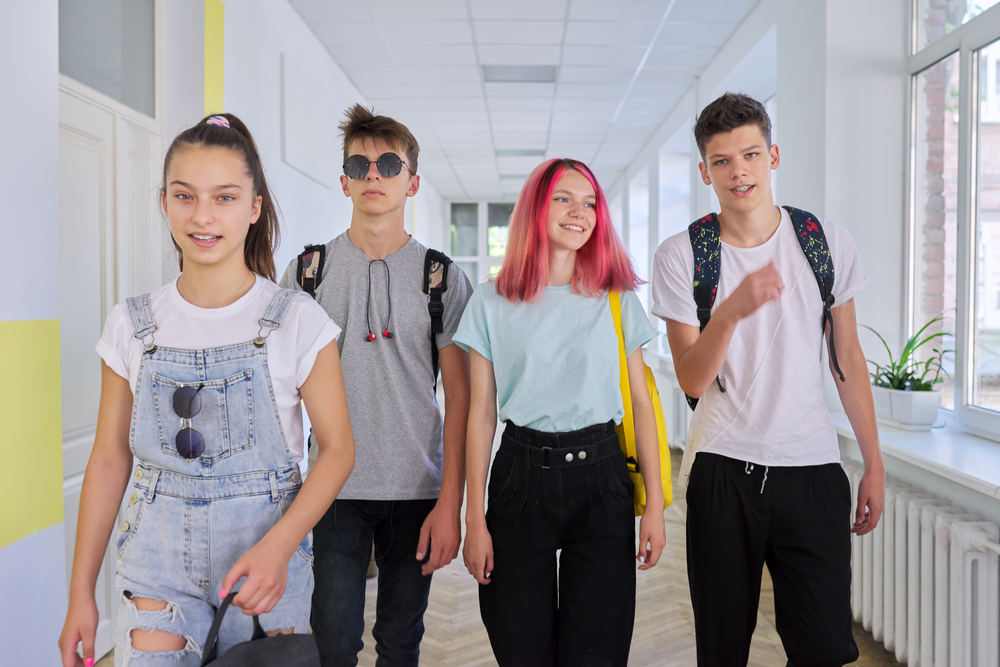 Group of teenage students walking together along school corridor, schoolchildren smiling and talking. Education, high school, adolescence concept