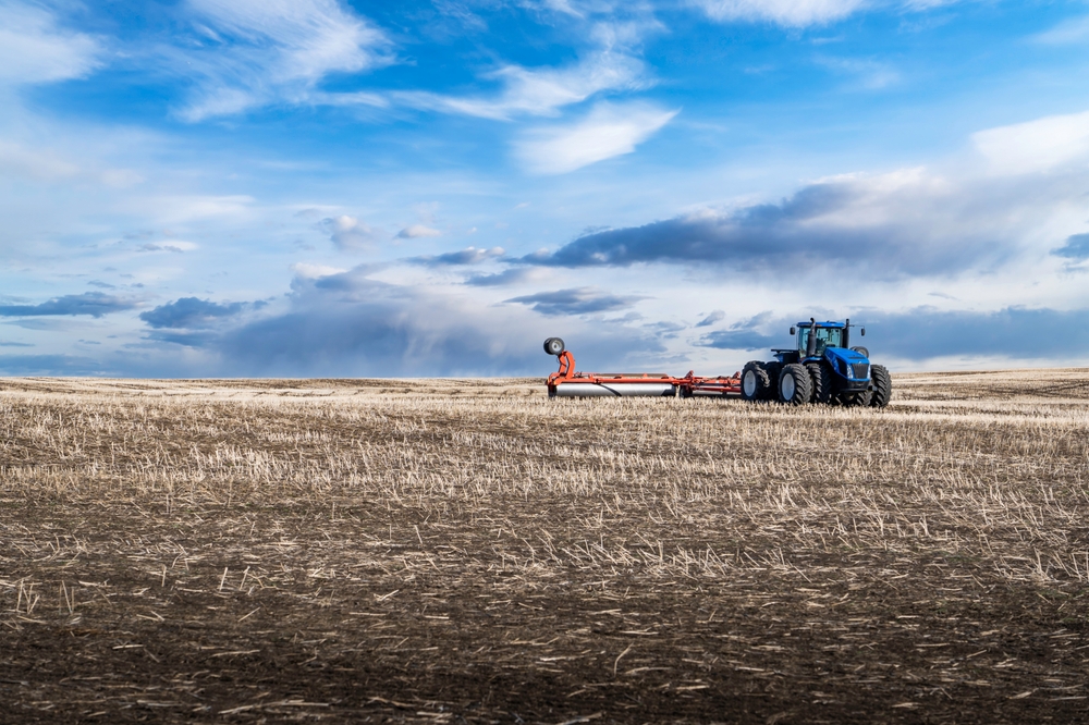 An eight wheel tractor pulling a plow across a tilled field with rolling hills in Rocky View County Alberta Canada under a dramatic cloudy sky.