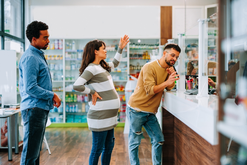 A pregnant woman is impatient and angry in a pharmacy queue annoyed with a customer ahead of her taking to long to finish shopping  with the pharmacist.