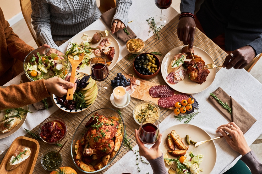 High angle view at diverse group of friends enjoying homemade food at festive dinner table with roasted turkey or chicken, copy space