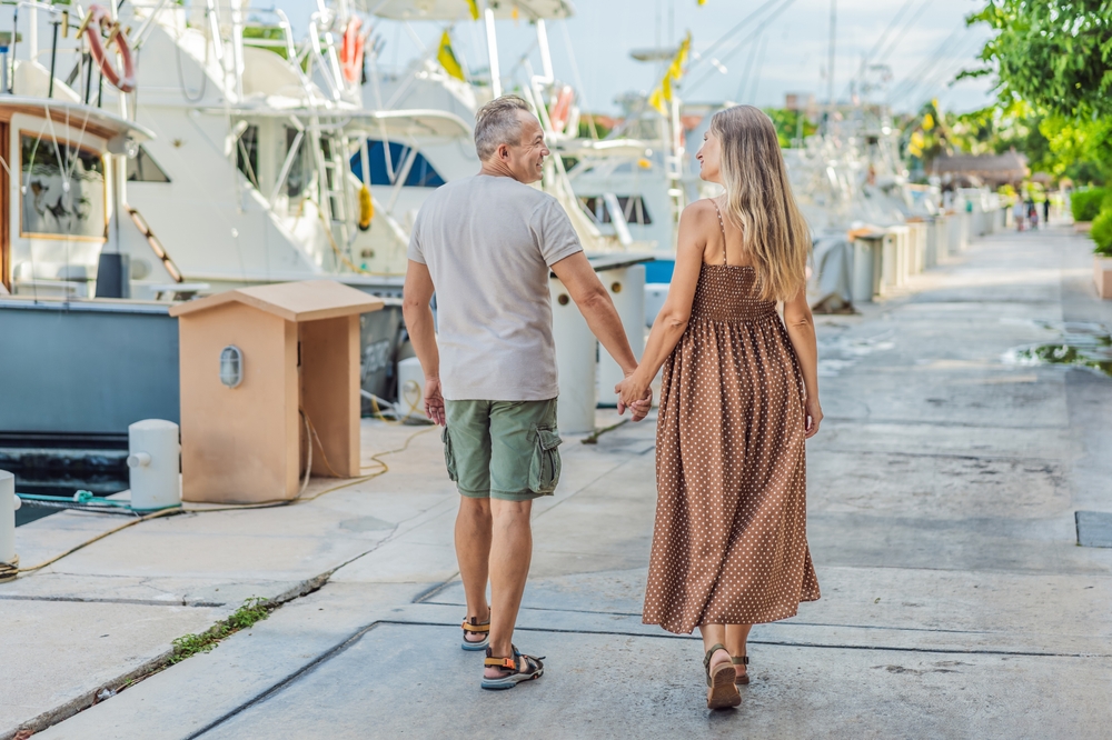 A happy, mature couple over 40, enjoying a leisurely walk on the waterfront, their joy evident as they embrace the journey of pregnancy later in life