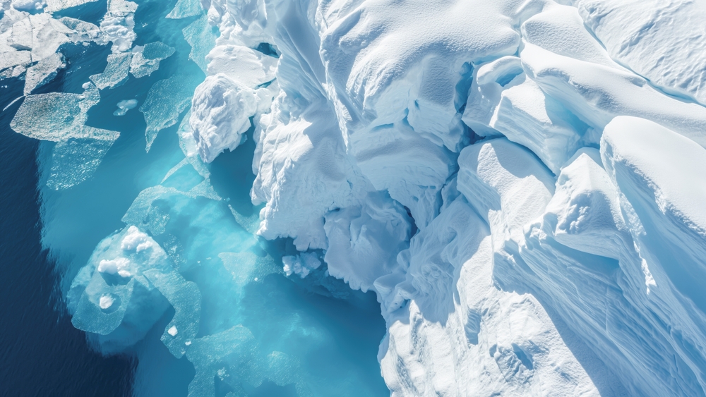 An aerial perspective showcases the dramatic melting icebergs of Antarctica, where the vivid blue sea claims the collapsing icy giants, a poignant visual testament to climate change