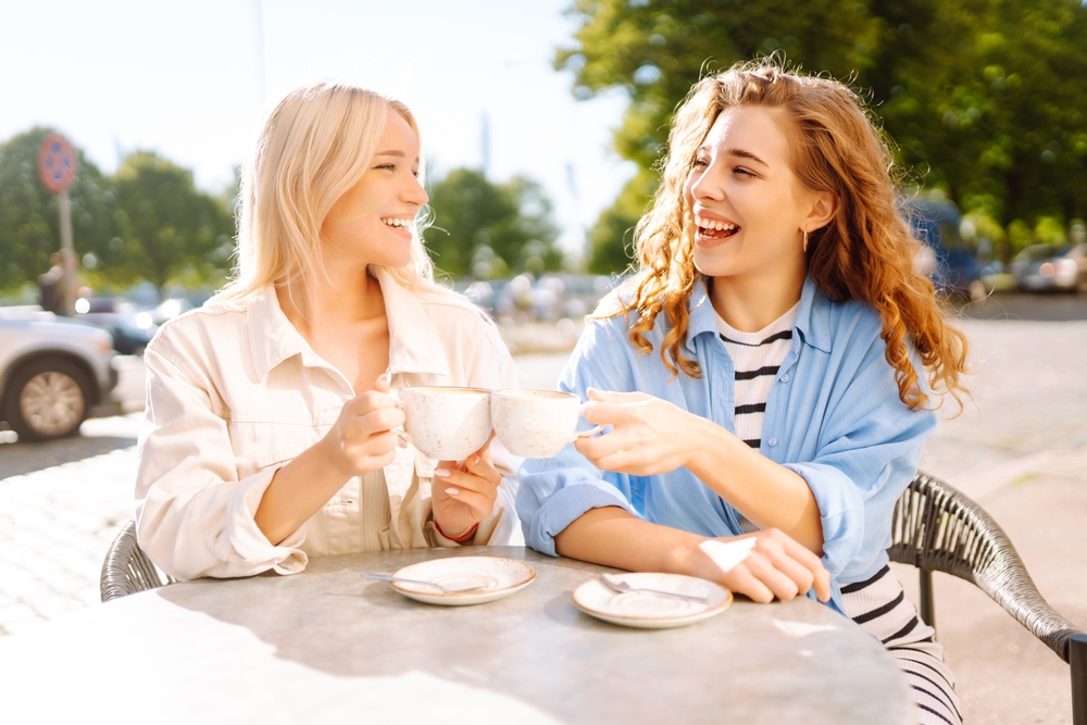 Friendship concept. Two girlfriends women eating breakfast in city cafe together while gossiping and spending free time.