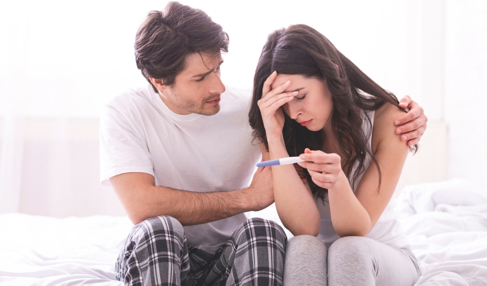 Couple dreaming to be parents. Upset man comforting his depressed wife with negative pregnancy test, free space