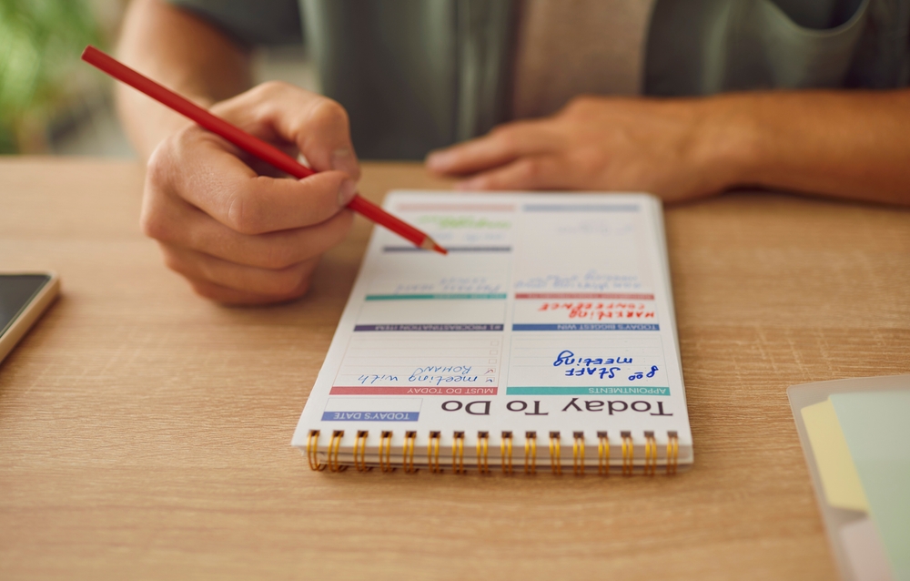 Man hands writing a detailed schedule, plan, and task list in notebook. His actions reveal a commitment to planning, utilizing the pages of calendar as a canvas for orchestrating the daily activities.