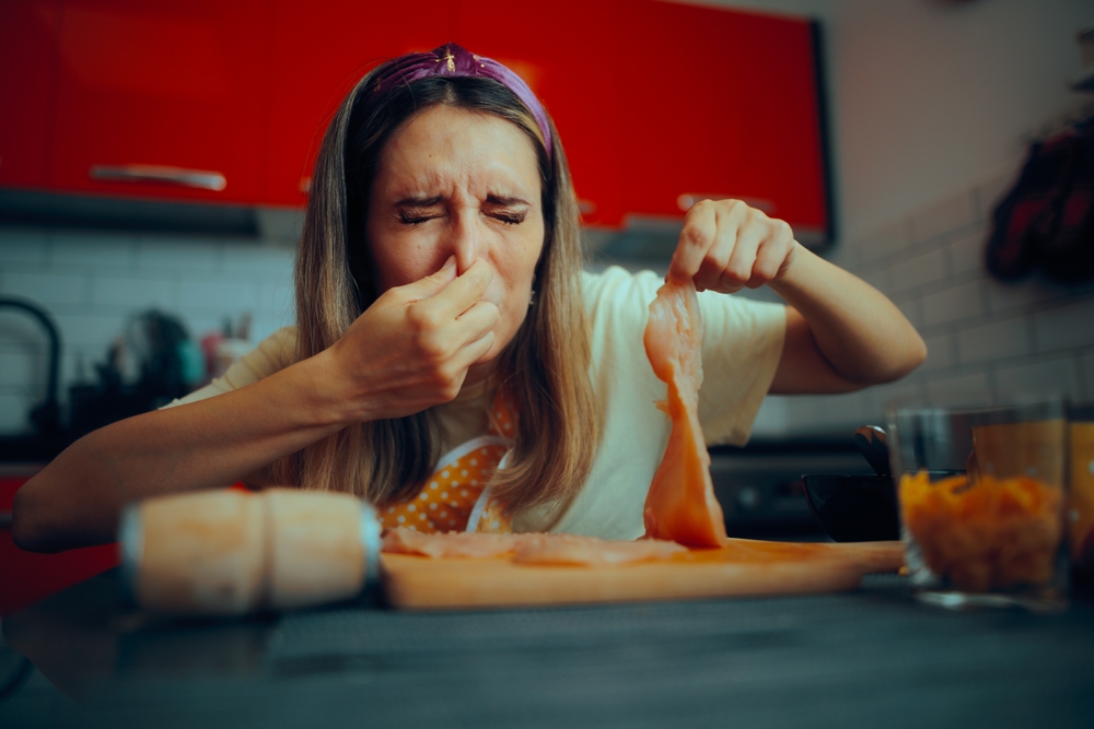Cooking Woman Holding Meat Feeling Disgusted by Its Smell
Person feeling nauseated because of poultry meat gone bad at home
