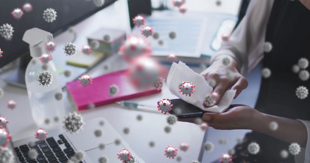 Image of covid 19 cells floating over woman wiping smartphone in office. workplace and business during covid 19 pandemic concept digitally generated image.