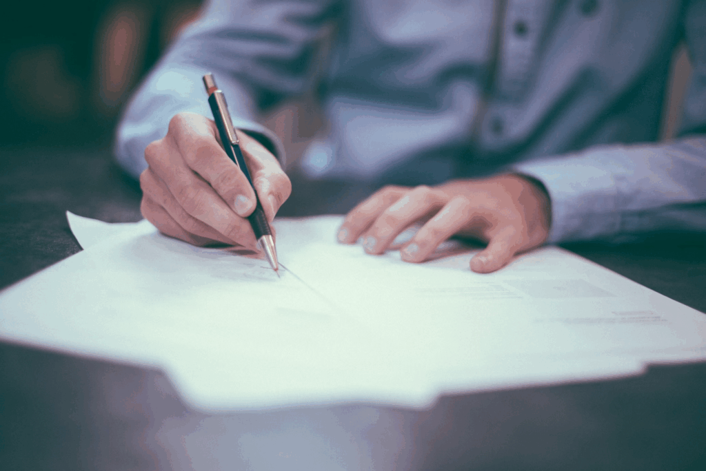 man writing on paper while wearing long sleeved shirt and holding pen